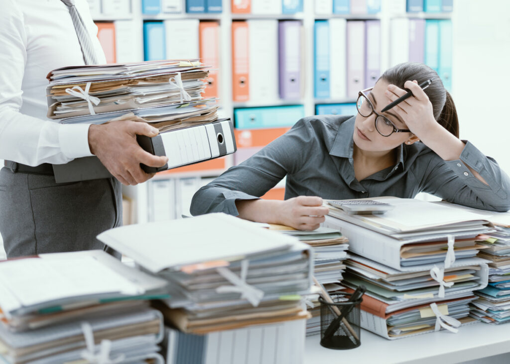 Empresária estressada no escritório sobrecarregada pelo trabalho e mesa cheia de arquivos por questões burocráticas.