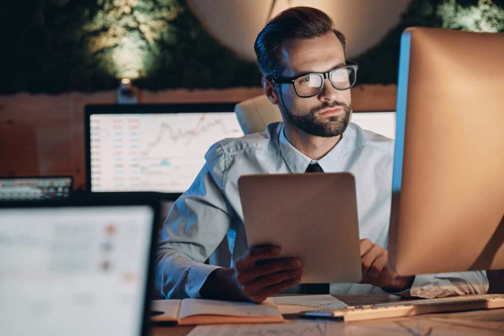 Homem de terno e gravata com tablet na mo e olhando para o computador pensando em como abrir empresa e negcios e ter lucro.